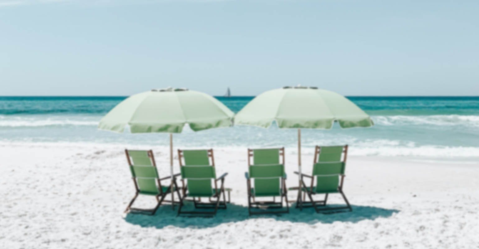 Sebuah foto buram kursi hijau di bawah payung di atas pasir pantai